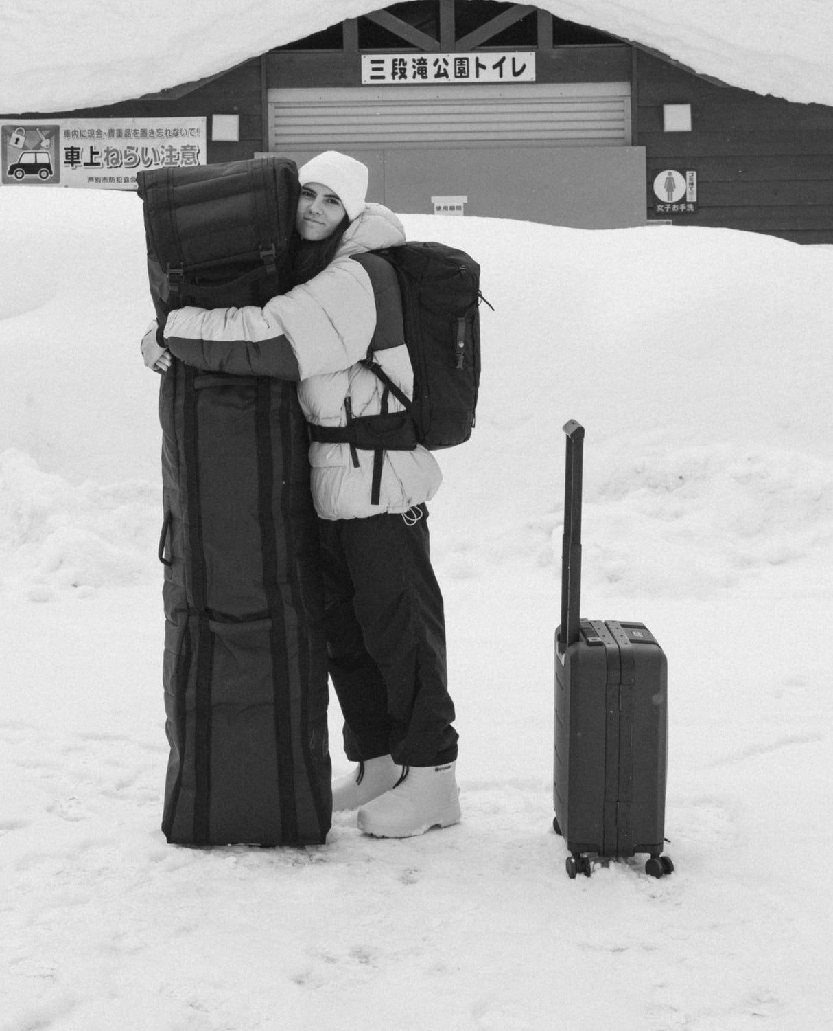 Skidåkare i vita Fubuki Niseko-vinterstövlar som kramar ett skidfodral i ett snöigt vinterlandskap.