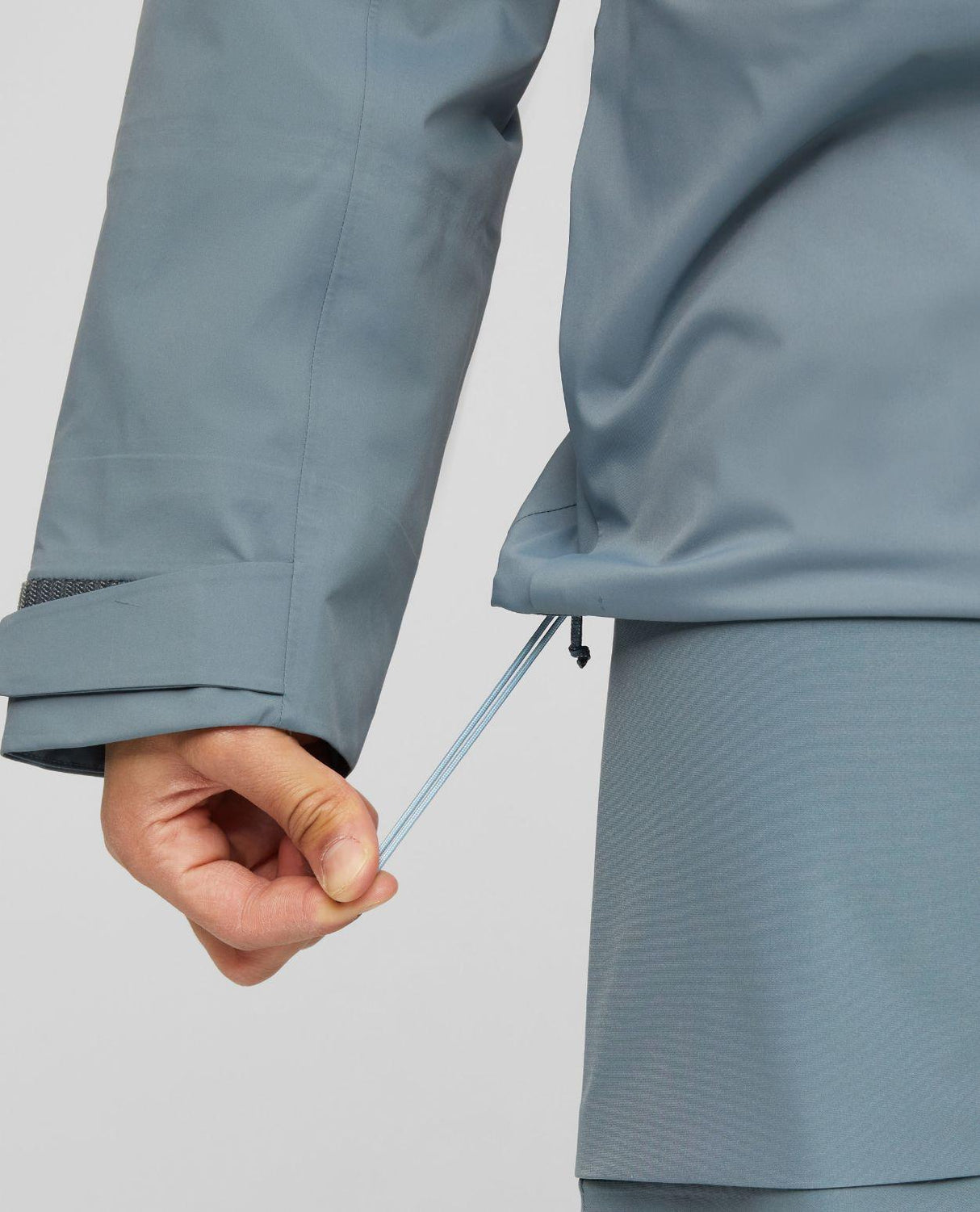 Mammut Haldigrat HS Hooded Jacket för herrar visar justering av dragsko i nederkant på den gråblå hardshelljackan.