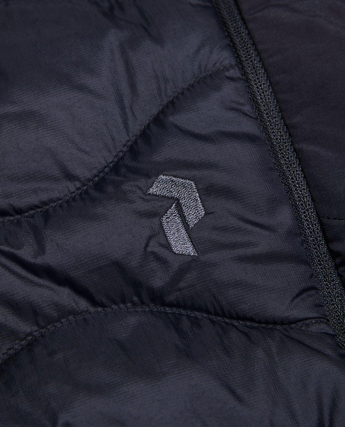 Närbild på Peak Performance Helium Down Shorts i svart med broderad logotyp.