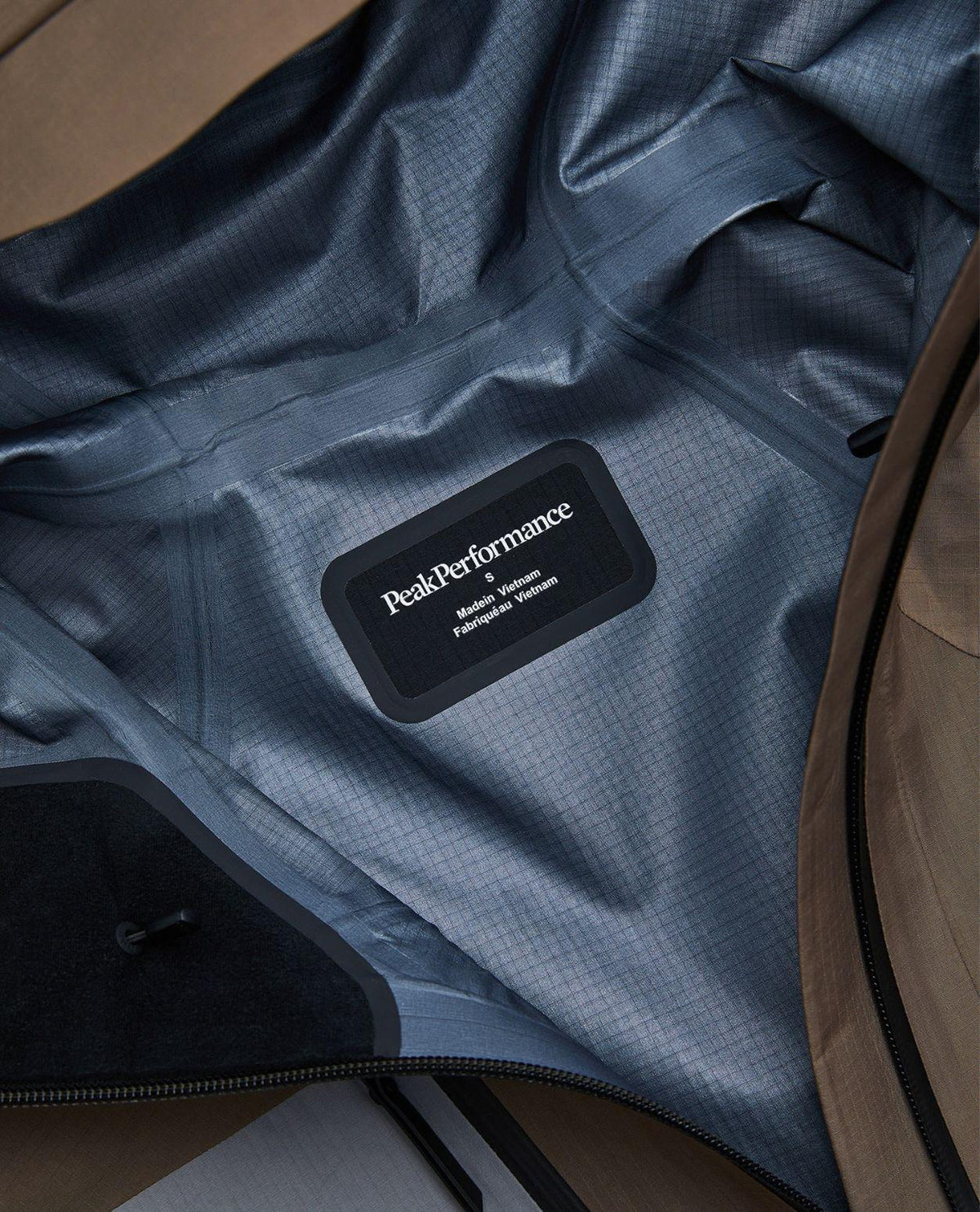 Närbild på insidan och logotypen i Peak Performance Vertical Gore-Tex Pro Jacket för dam i färgen Terrain Tan/Lt Grey.
