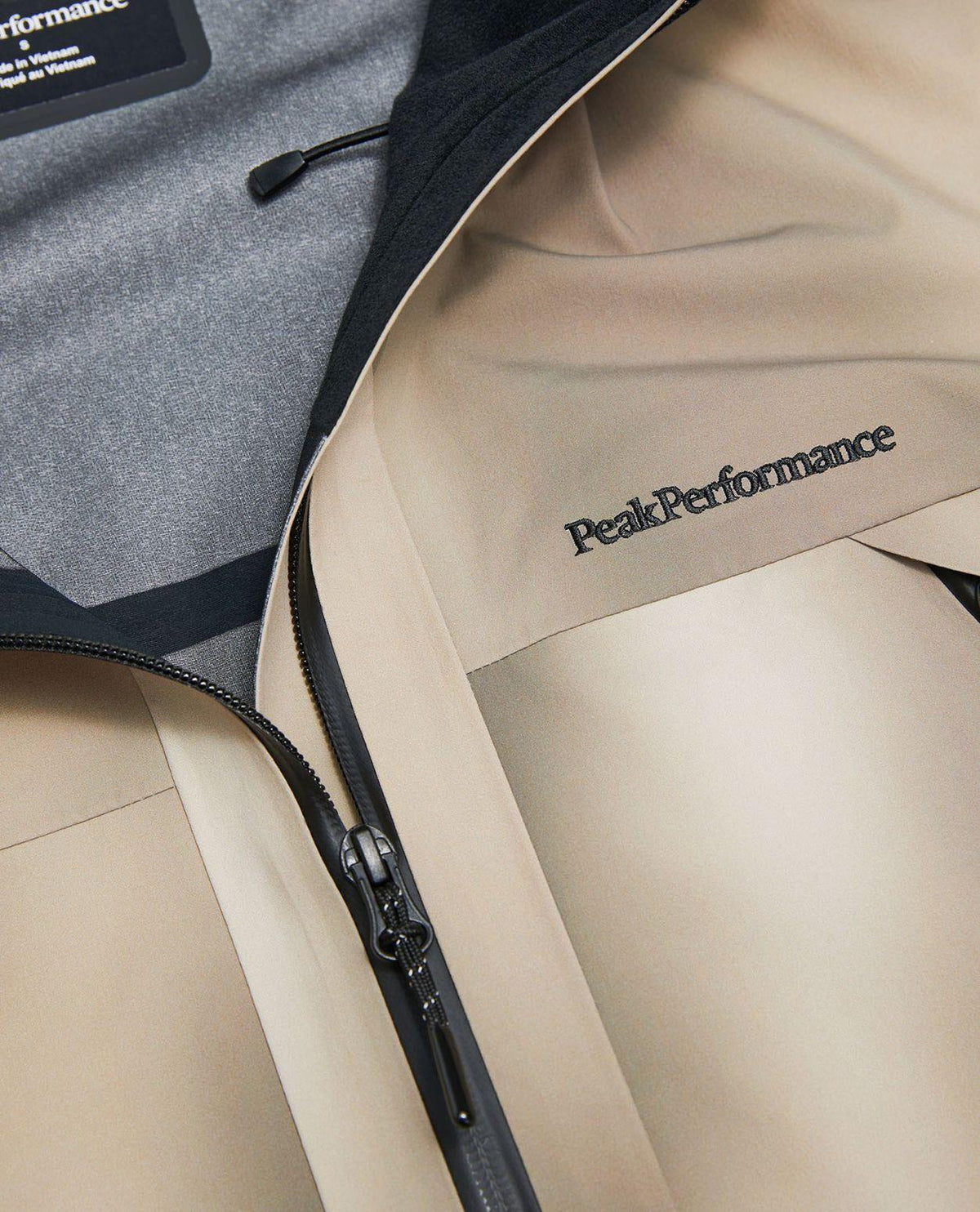 Närbild på Peak Performance Edge 3L AOP skidjacka dam i färgen 336 Beam Fade med broderad logotyp och dragkedja.