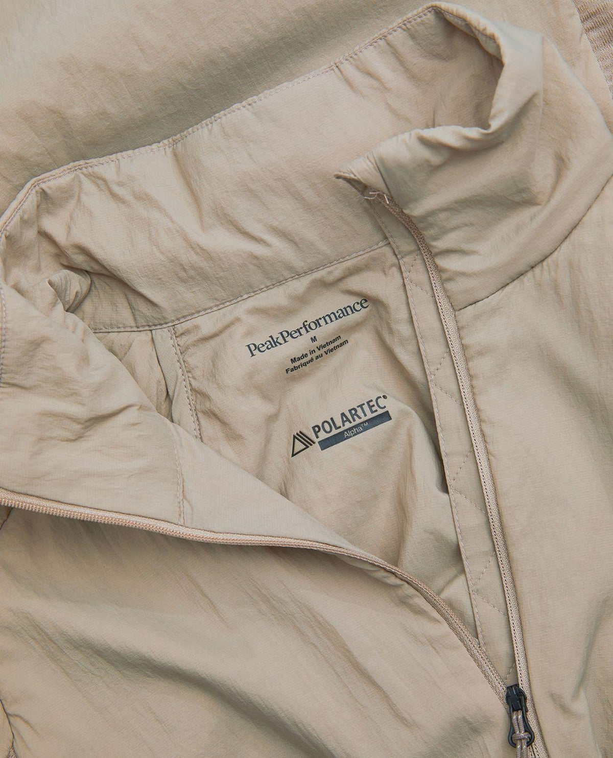 Närbild på insidan och kragen av Peak Performance Freelight Hybrid Liner Men i färgen Avid Beige med Polartec Alpha-detalj.