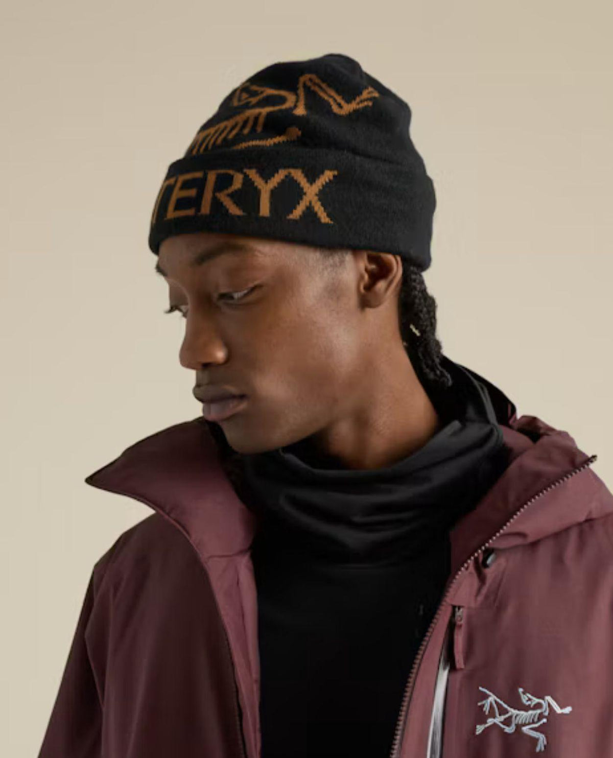 Person som bär en svart Arc'teryx Bird Word Toque-mössa med guldfärgat mönster.
