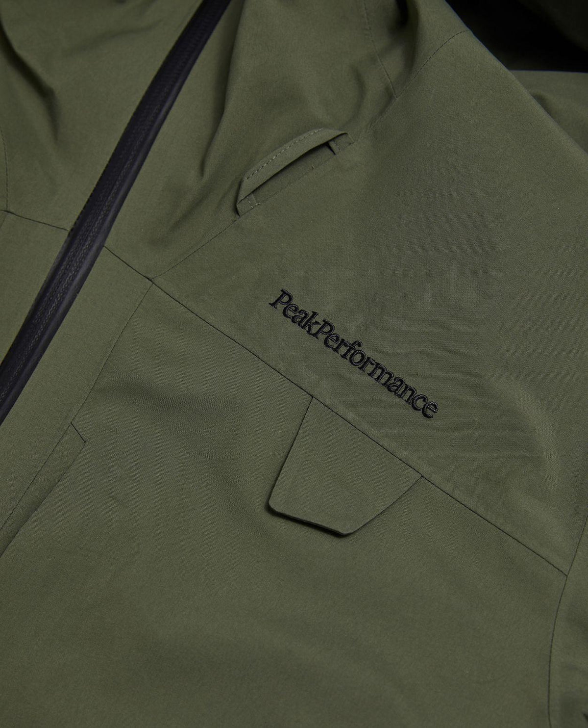 Närbild på bröstpartiet av Peak Performance Alpine Gore-Tex 3L Jacket i färgen Pine Needle med broderad logo.