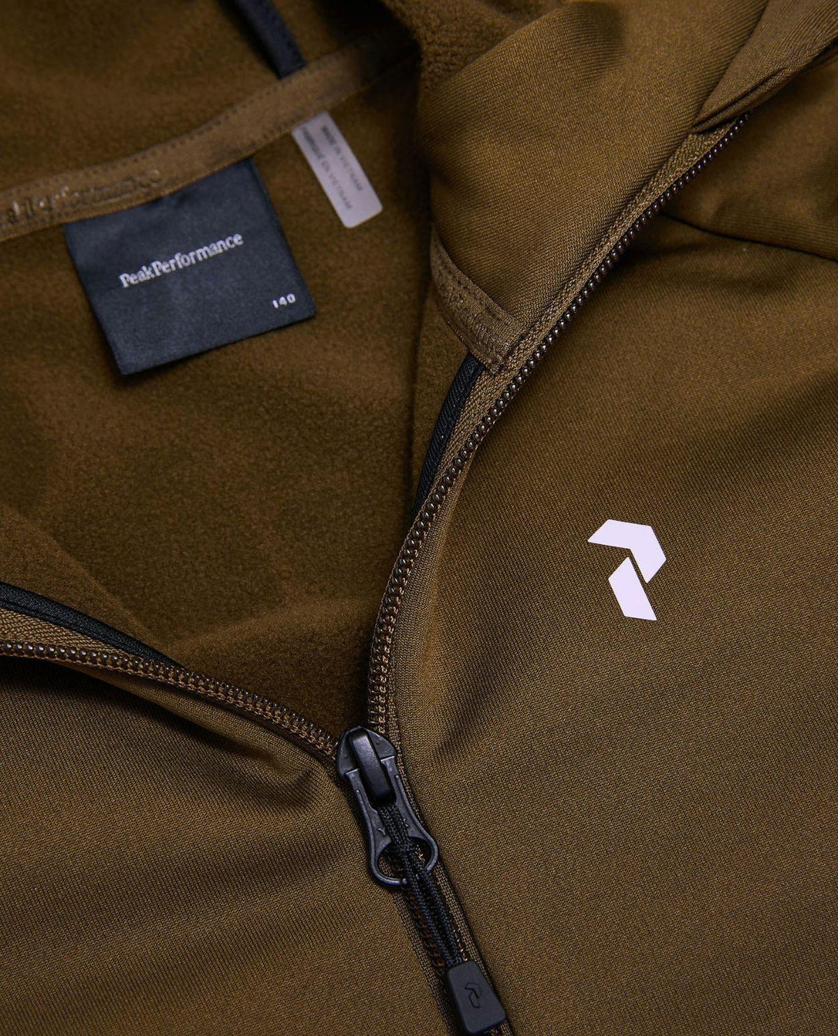 Peak Performance Rider Essentials Zip Hood Junior i grön Meadow Moss visar bröstdetaljer och logotyp.