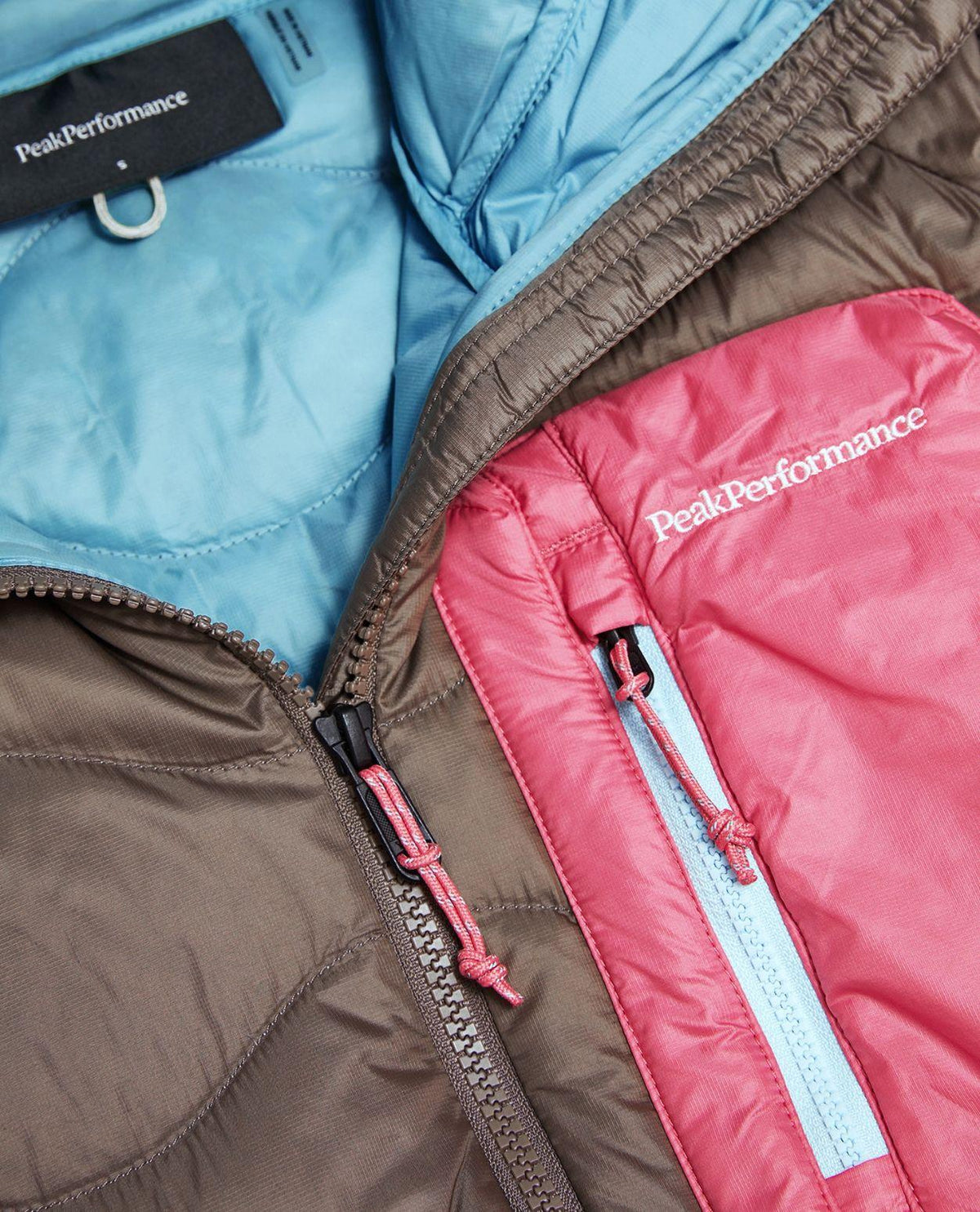 Närbild på bröstficka och dragkedja på Peak Performance Helium Utility Down Hood Jacket i dammodell.