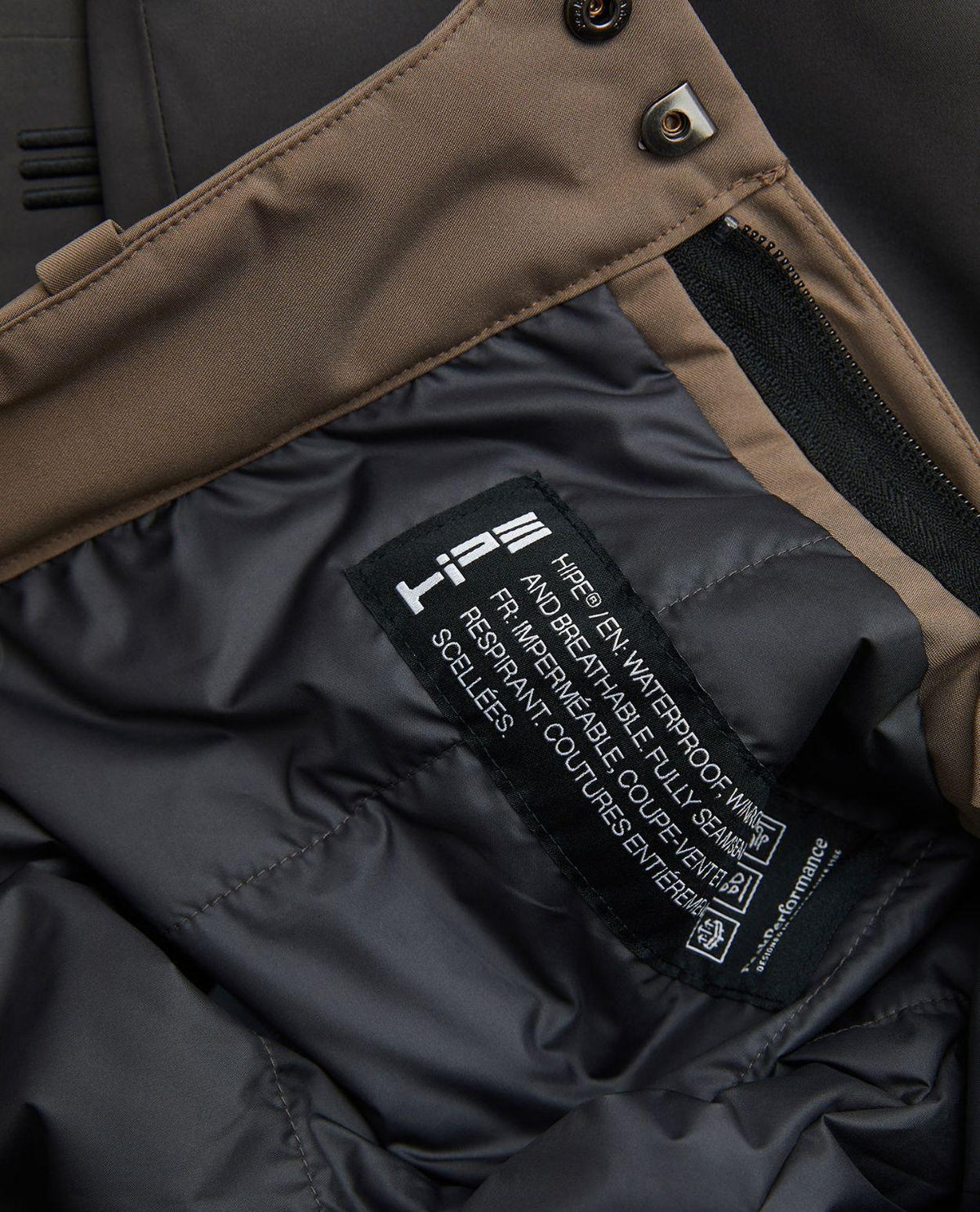 Detaljbild på insidan och etiketten för Peak Performance Gravity Insulated Pants Junior i brunt.