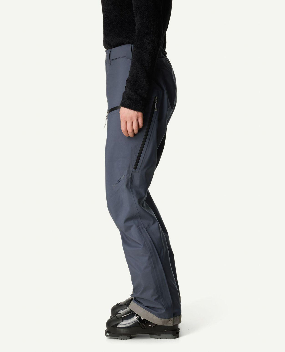 Houdini Ride Pants II dam i blått sett från sidan på en skidåkare med pjäxorna på.