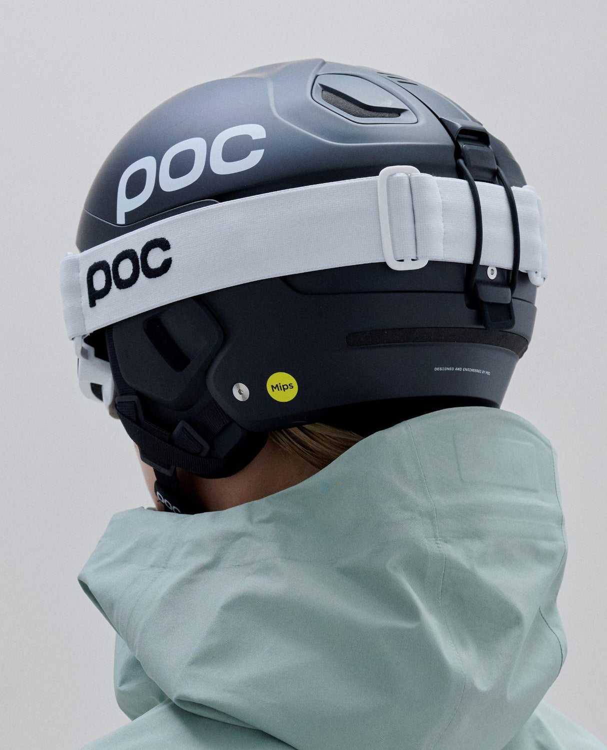 Baksida av POC Nexal Mid skigoggles i vitt med matchande POC-skidhjälm och ljusgrön jacka.