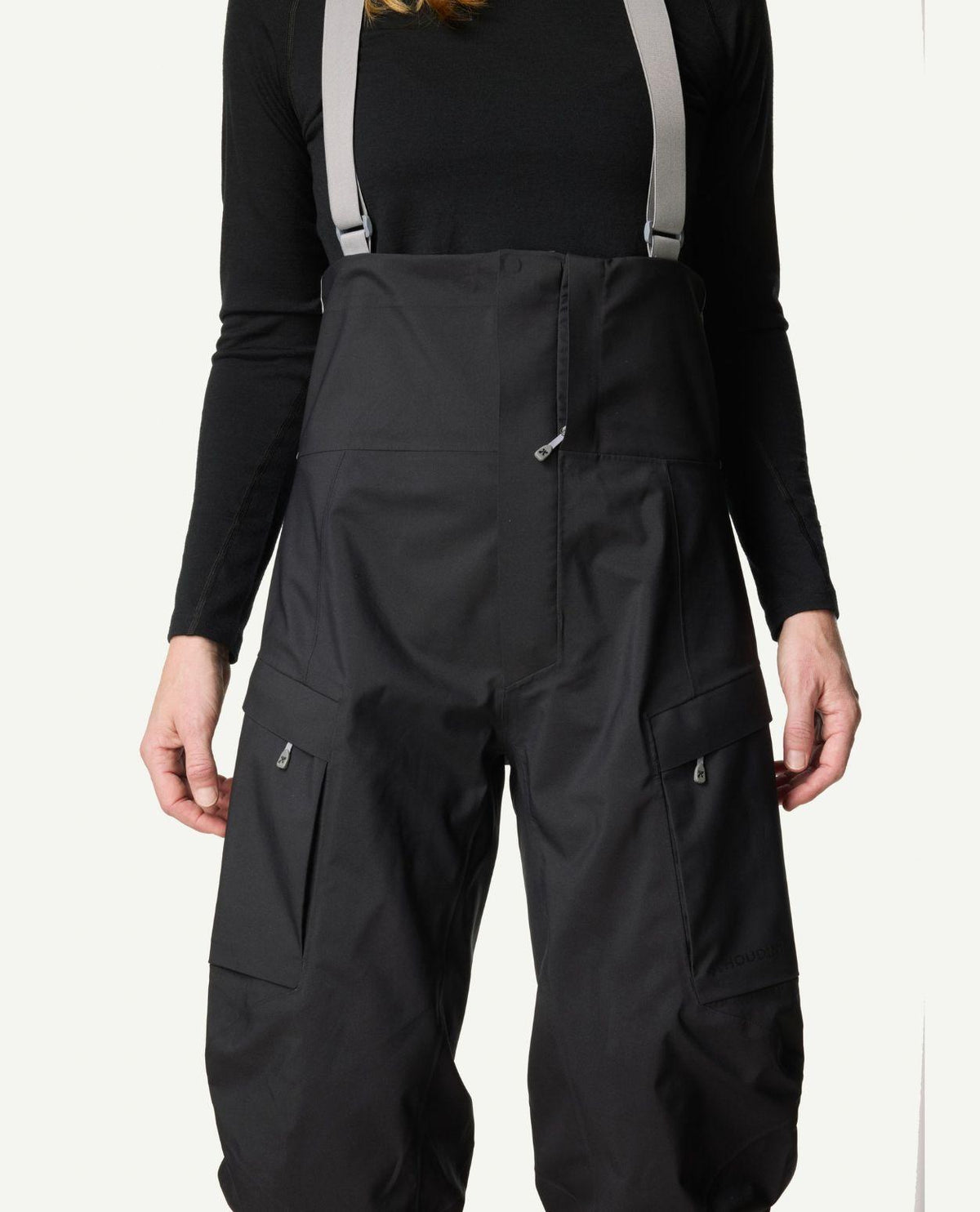 Närbild på Houdini Rollercoaster Bib Pants II skidbyxor för dam i svart med grå hängslen och benfickor.