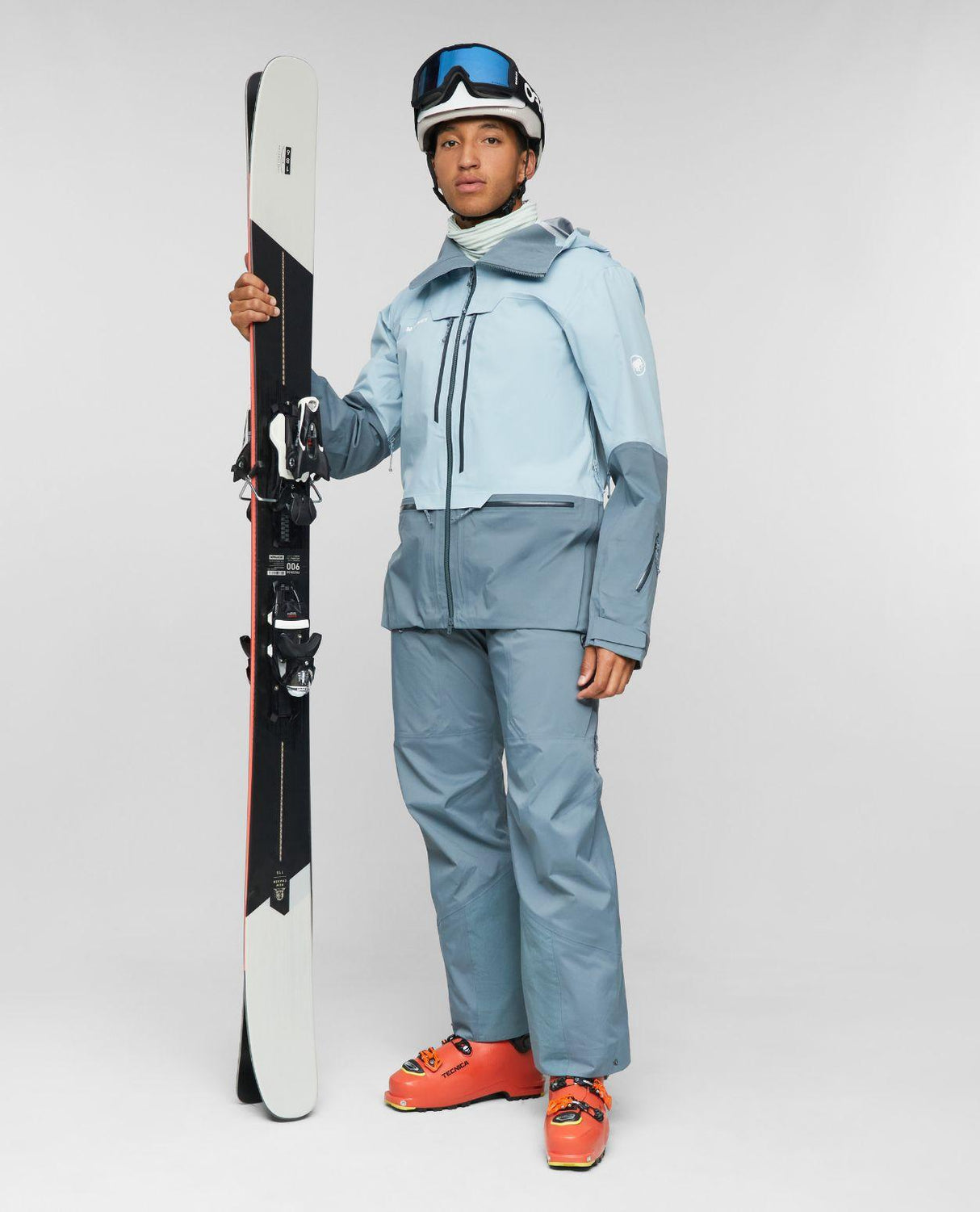 Skidåkare i Mammut Haldigrat HS Bib Pants och matchande jacka i färgen Strata som håller i ett par alpinskidor.