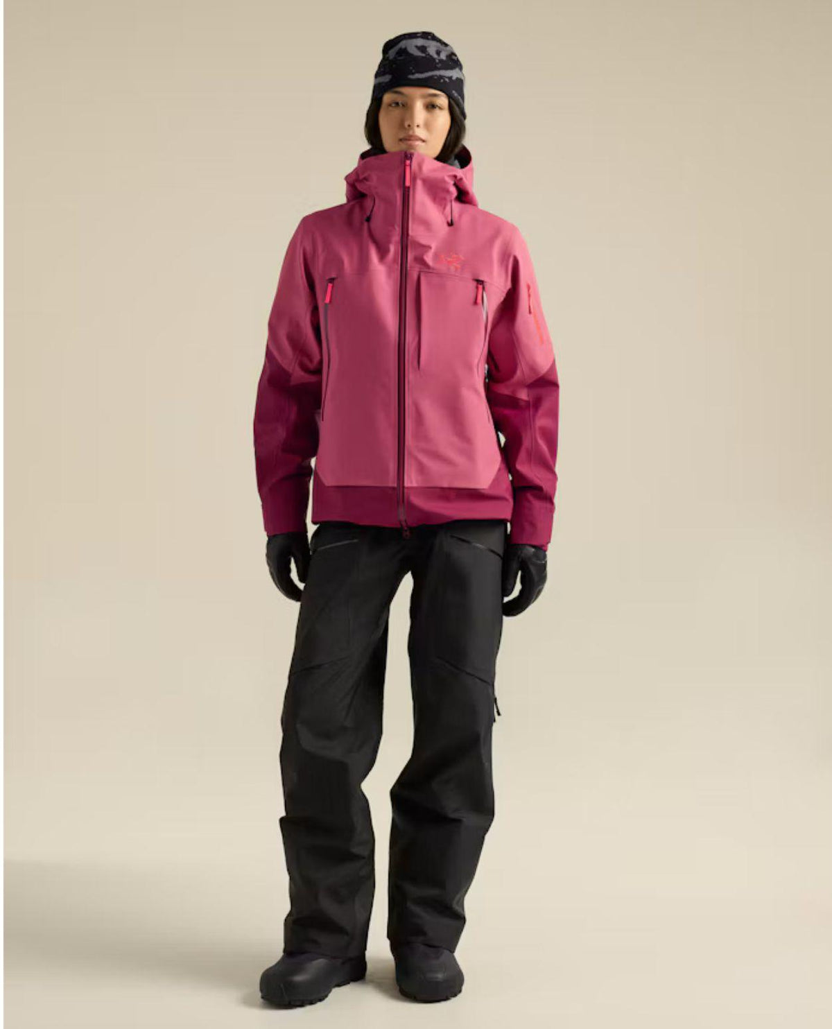 En kvinnlig skidåkare bär en rosa skidjacka från Arc'teryx samt svarta byxor, handskar och mössa.