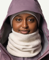 Person bär Houdini Lykan Neck Gaiter i beige färg runt halsen under en lila skidjacka.