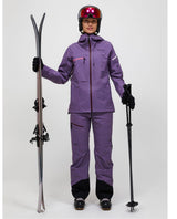 Skidåkare i lila Peak Performance Alpine Gore-Tex 3L Jacka och matchande skidbyxor håller i skidor och stavar.