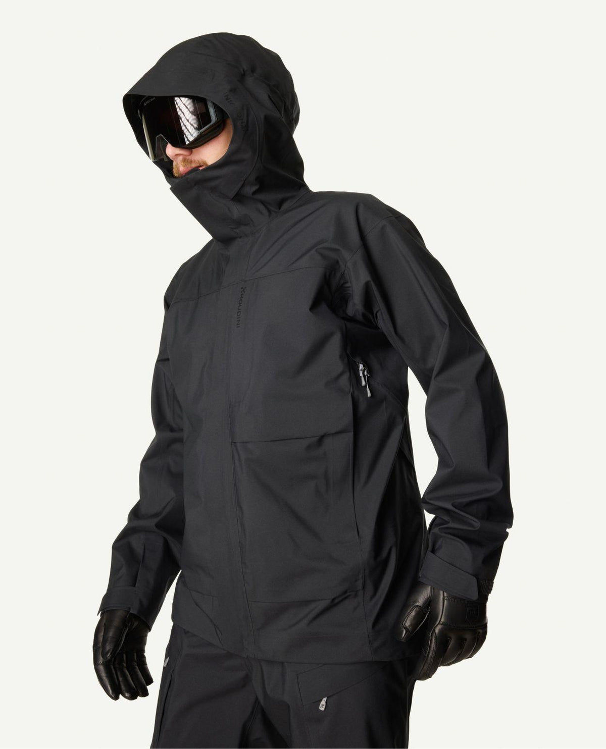 Skidåkare i profil bärandes en svart Houdini Rollercoaster Jacket II med huva uppdragen och skidglasögon.