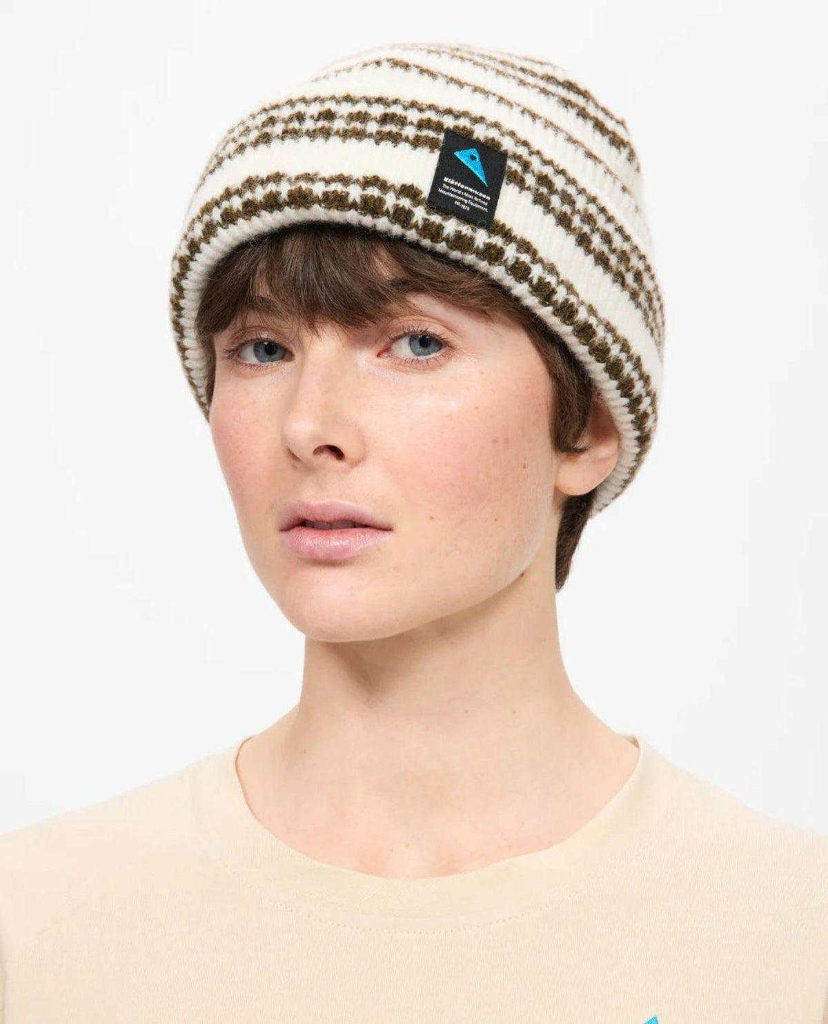 Klättermusen Runa Bandr Beanie i snövitt utförande med uppvikt kant och mönstrad stickning, buren av en person.