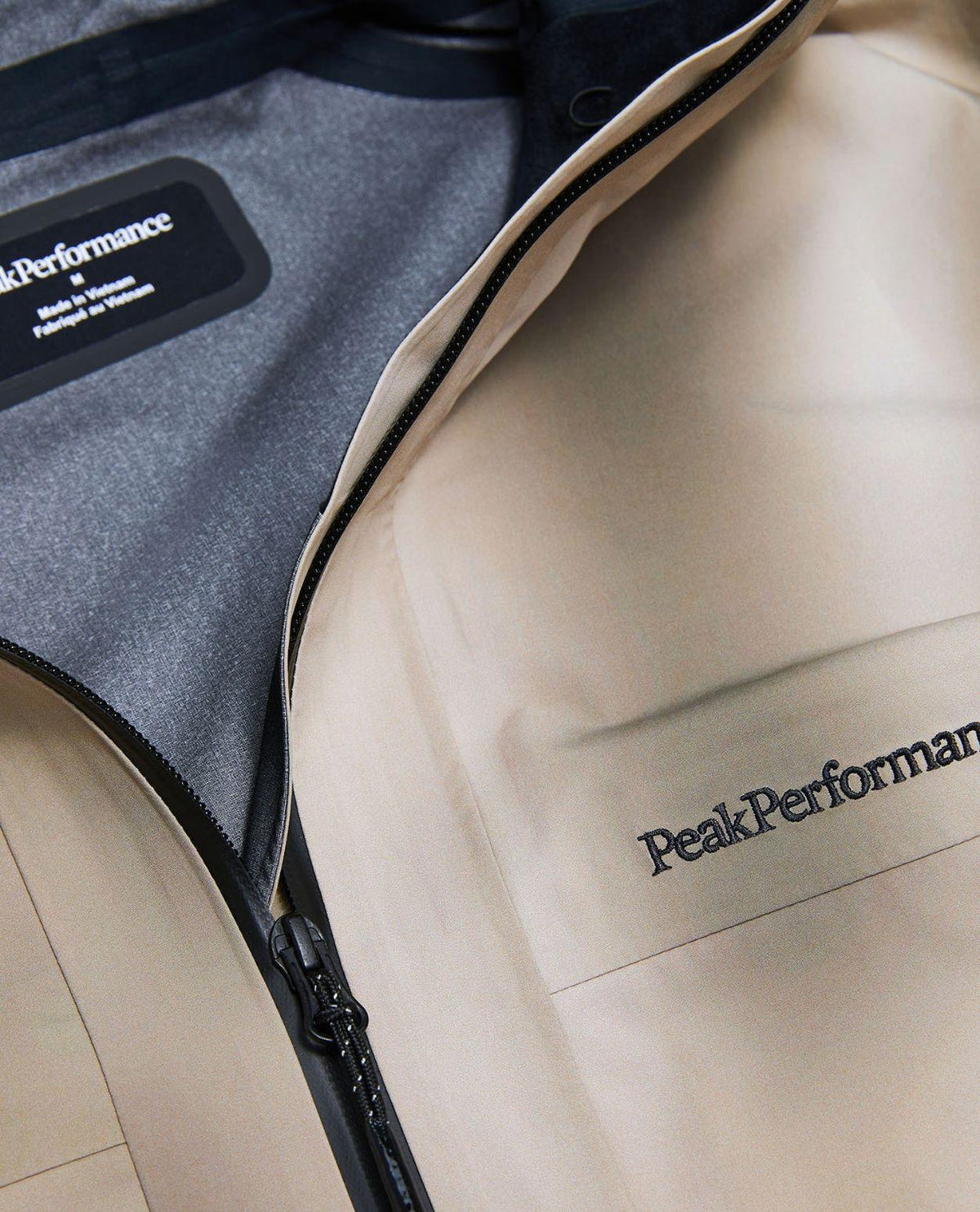 Närbild på Peak Performance Edge 3L AOP skidjacka för herr i färgen beam fade som visar dragkedja och tryckt logotyp.