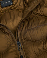 Närbild på Peak Performance Helium Down Vest Junior i brun färg med broderad logo och dragkedja.