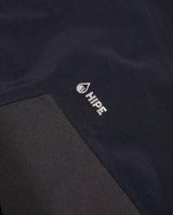Närbild på det svarta HIPE-materialet och logotypen på Peak Performance Edge 3L Bib Pants Women.
