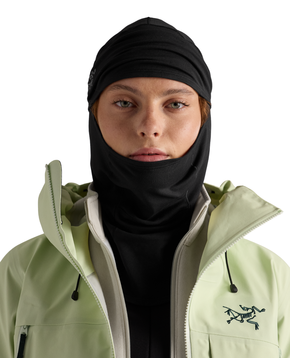 Person bär en svart Arc'teryx Rho Balaclava i ljusgröna skidkläder.