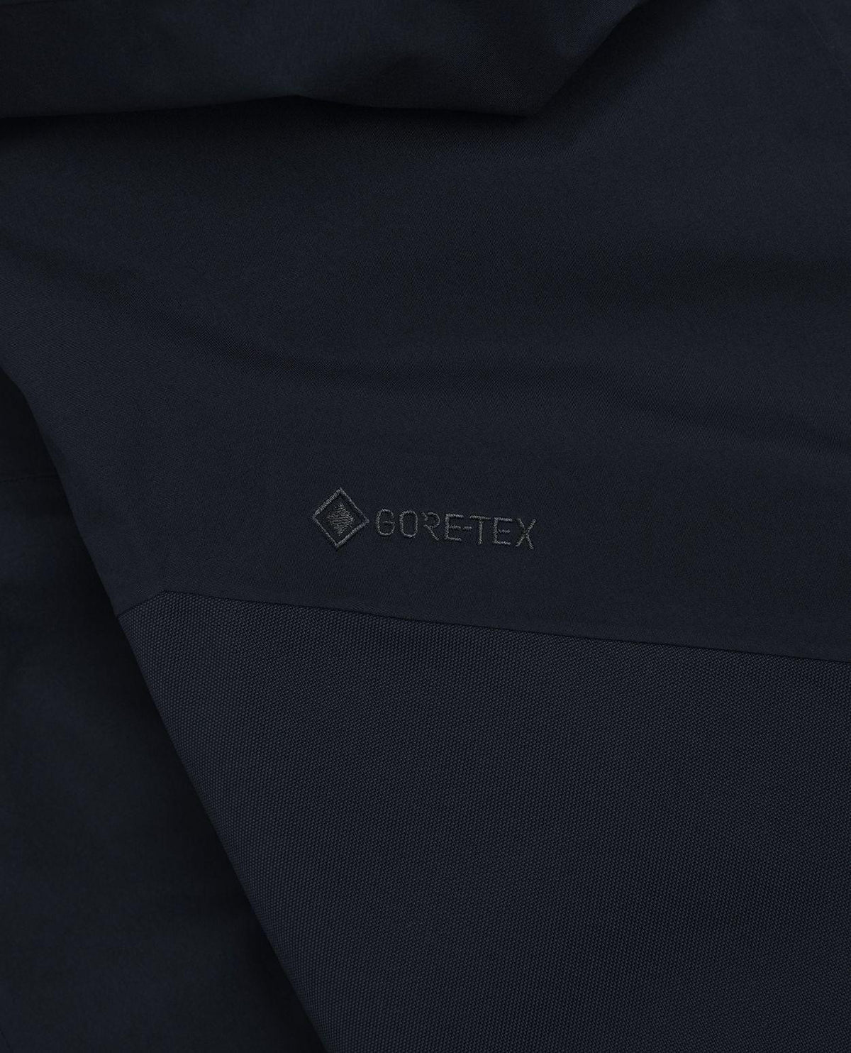 Detaljbild på den svarta Gore-Tex-logotypen på Peak Performance Alpine Gore-Tex Insulated skidbyxor för herr.