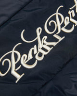 Närbild på den broderade Peak Performance-logotypen på den svarta dam skidjackan.