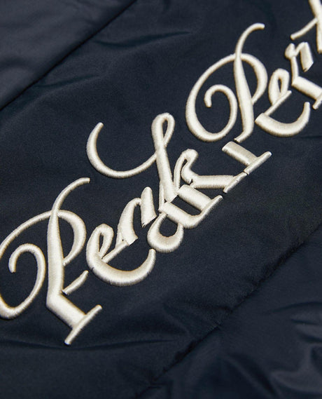 Närbild på den broderade Peak Performance-logotypen på den svarta dam skidjackan.