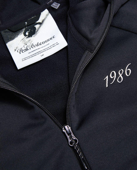 Närbild på den svarta Peak Performance 40Y Rider Zip Hood dam med dragkedja och broderat årtal.