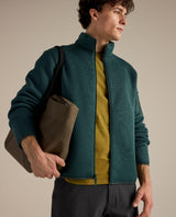 Arc'teryx Covert Cardigan i mörkt jadegrönt fleecematerial bärs av en man som håller en väska.