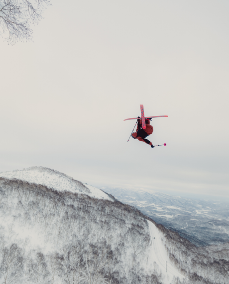 En skidåkare som gör ett hopp i luften över ett snöklätt berg med Salomon S/Lab QST X offpistskidor.