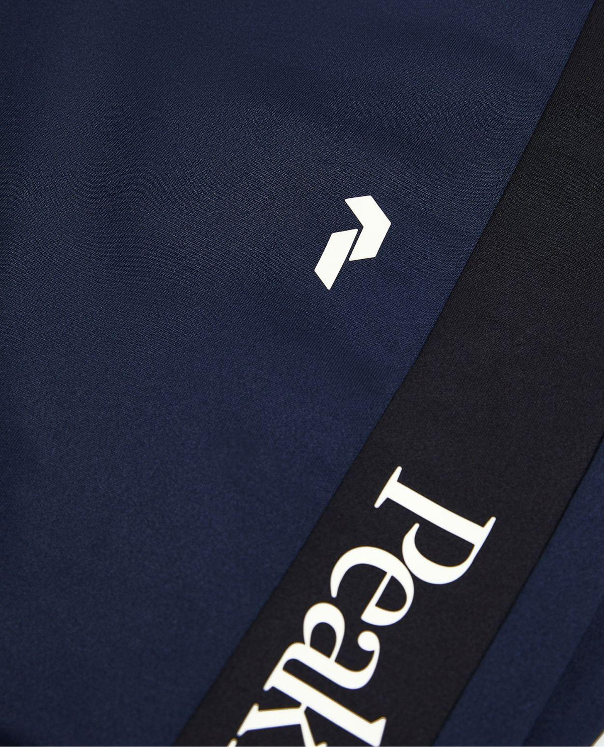 Närbild på Peak Performance Rider Essentials Pants i blått och svart med tydlig logotyp.