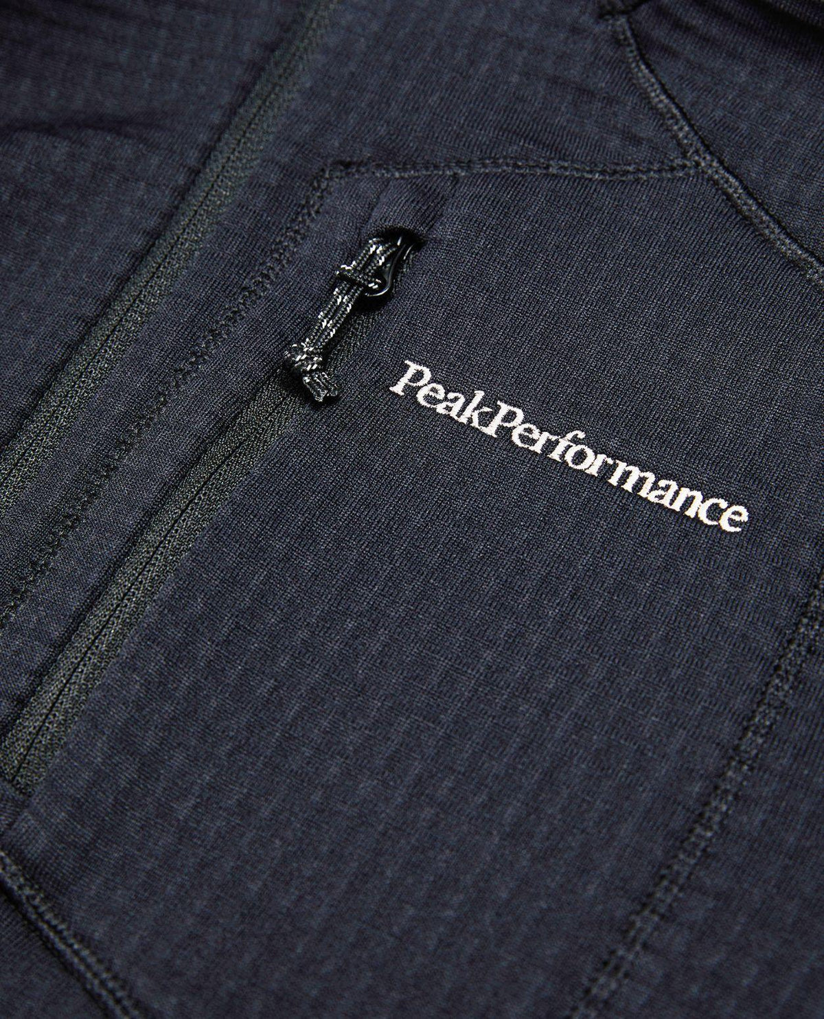 Närbild på bröstpartiet av Peak Performance Trail Polartec Zip Hood i svart med broderad logotyp och dragkedja.