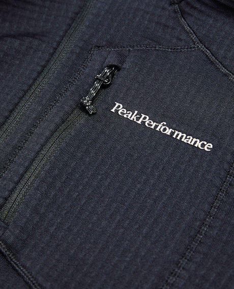 Närbild på bröstpartiet av Peak Performance Trail Polartec Zip Hood i svart med broderad logotyp och dragkedja.