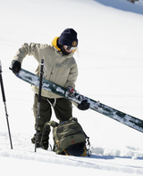 Skidåkare i snöigt fjällandskap som förbereder utrustning för toppturen med skidor och stavar.