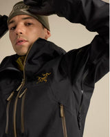 Man i svart Arc'teryx Rush Jacket med guldfärgade dragkedjor och logotyp.