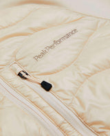 Närbild på Peak Performance Helium Down Hybrid Hood för damer i färgen sand fog med broderad logotyp och dragkedja.