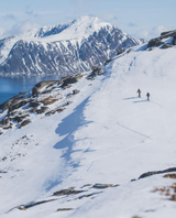 Två skidåkare på tur i ett storslaget snöklätt fjälllandskap med hav i bakgrunden med Armada Locator 96.