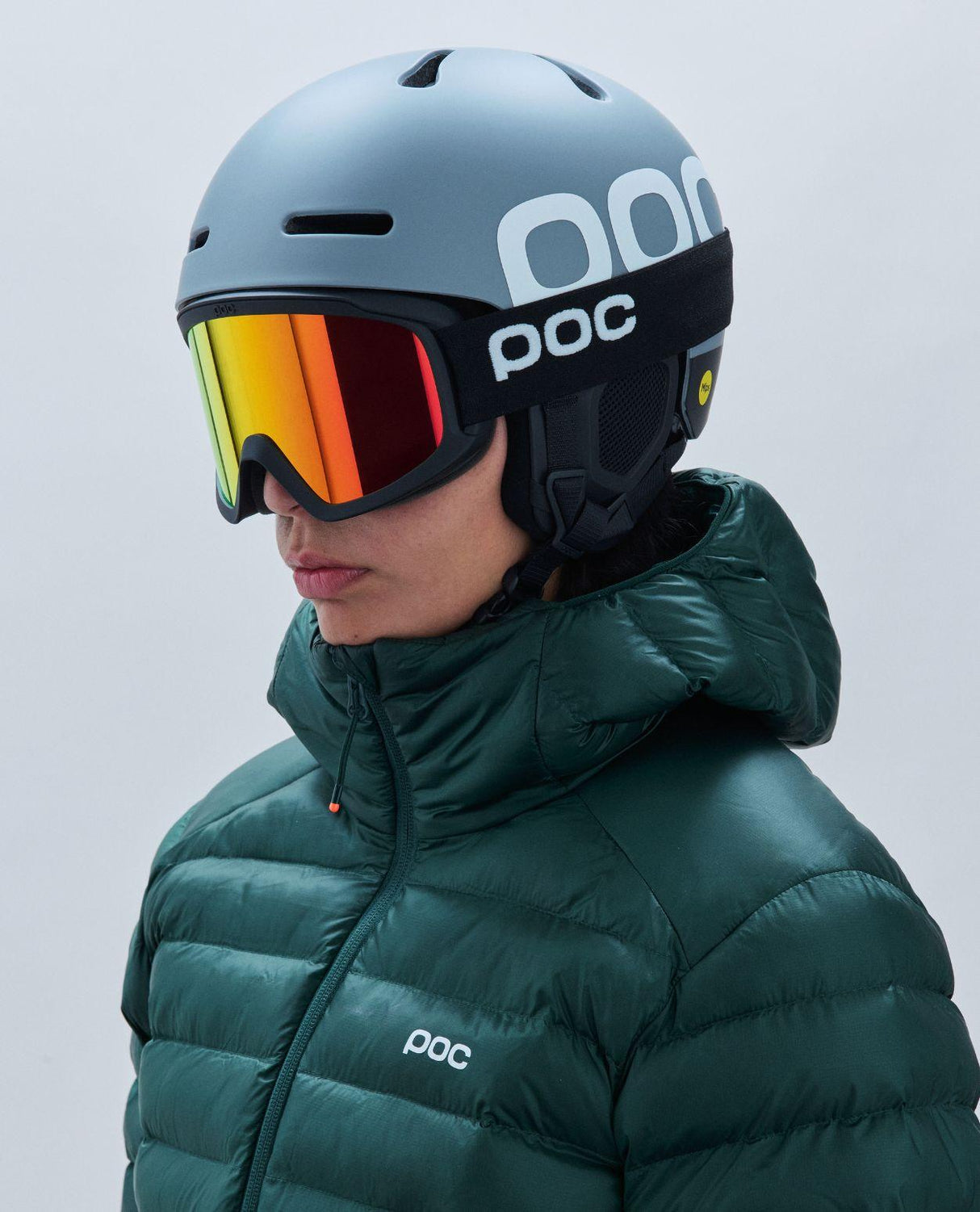 POC Opsin skidglasögon med svart ram och orange spegellins på skidentusiast iförd hjälm och grön jacka.