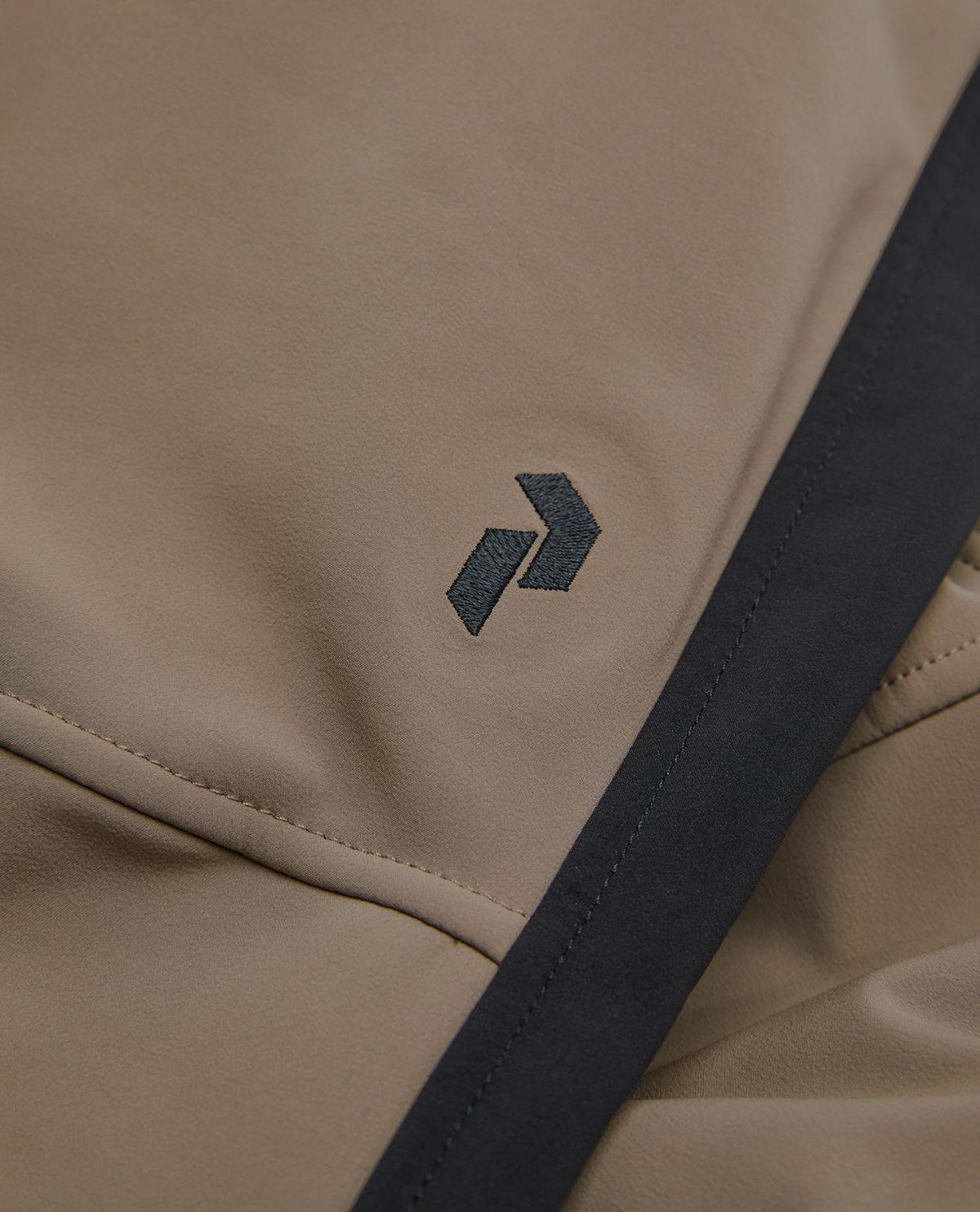 Detaljbild på broderad logotyp på Peak Performance Stretch Bib Pants dam i färgen Terrain Tan/Black.