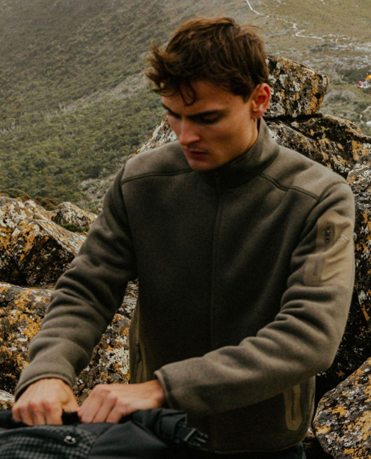 Man i naturmiljö bärandes Arc'teryx Covert Cardigan i färgen Mongoose Heather.