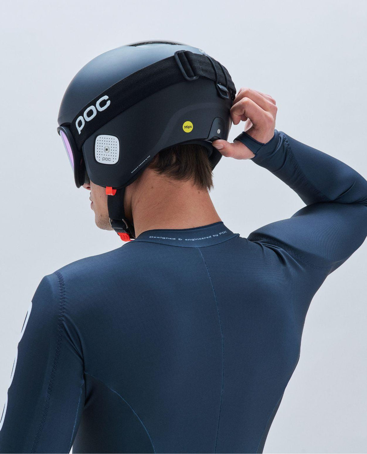 En person som justerar passformen med Race Lock på den svarta POC Skull Dura Comp MIPS-tävlingshjälmen bakifrån.