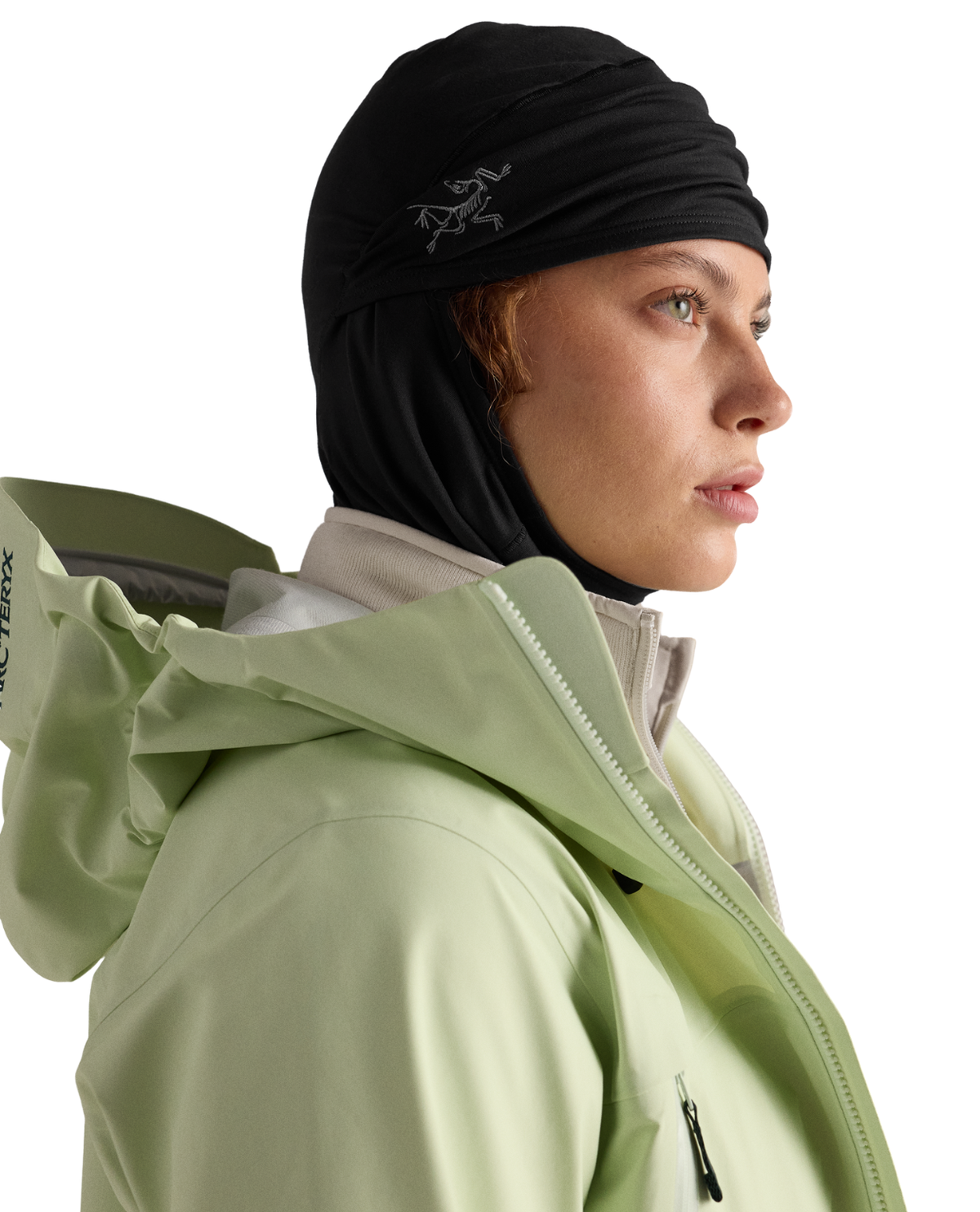 Arc'teryx Rho Balaclava i svart som bärs neddragen under hakan med en ljusgrön skaljacka för skidåkning.