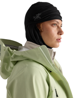 Arc'teryx Rho Balaclava i svart som bärs neddragen under hakan med en ljusgrön skaljacka för skidåkning.