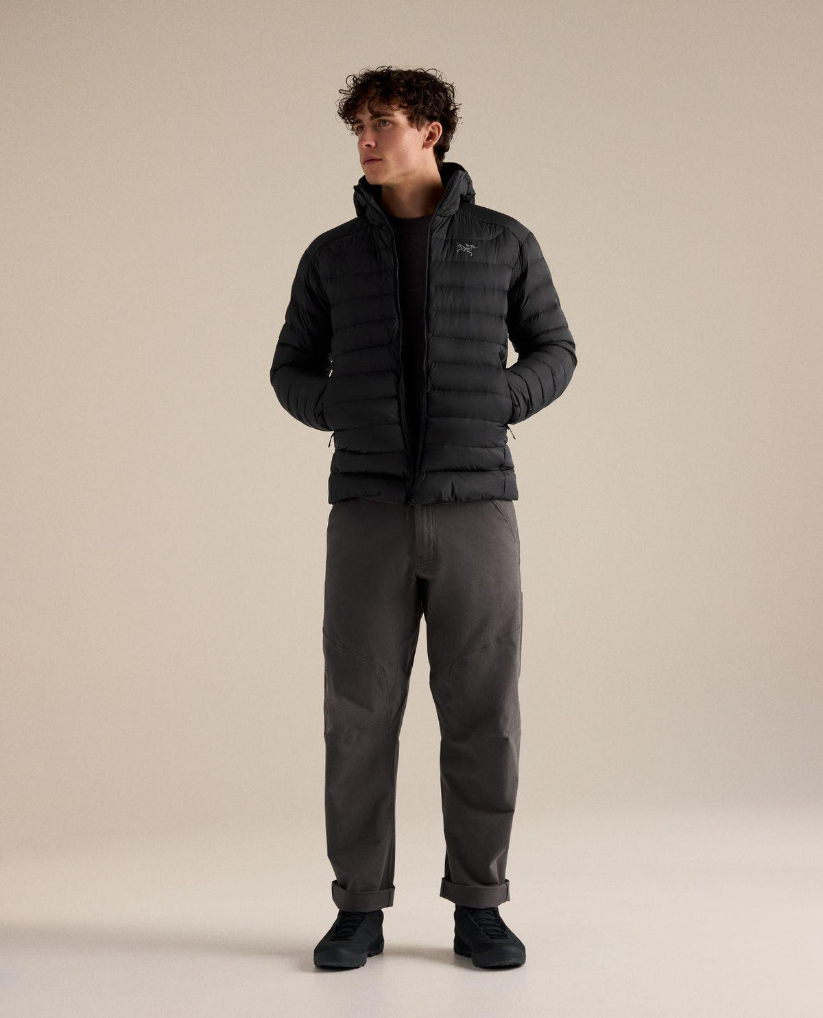 Man i svart Arc'teryx Cerium Hoody dunjacka med huva och händerna i fickorna.