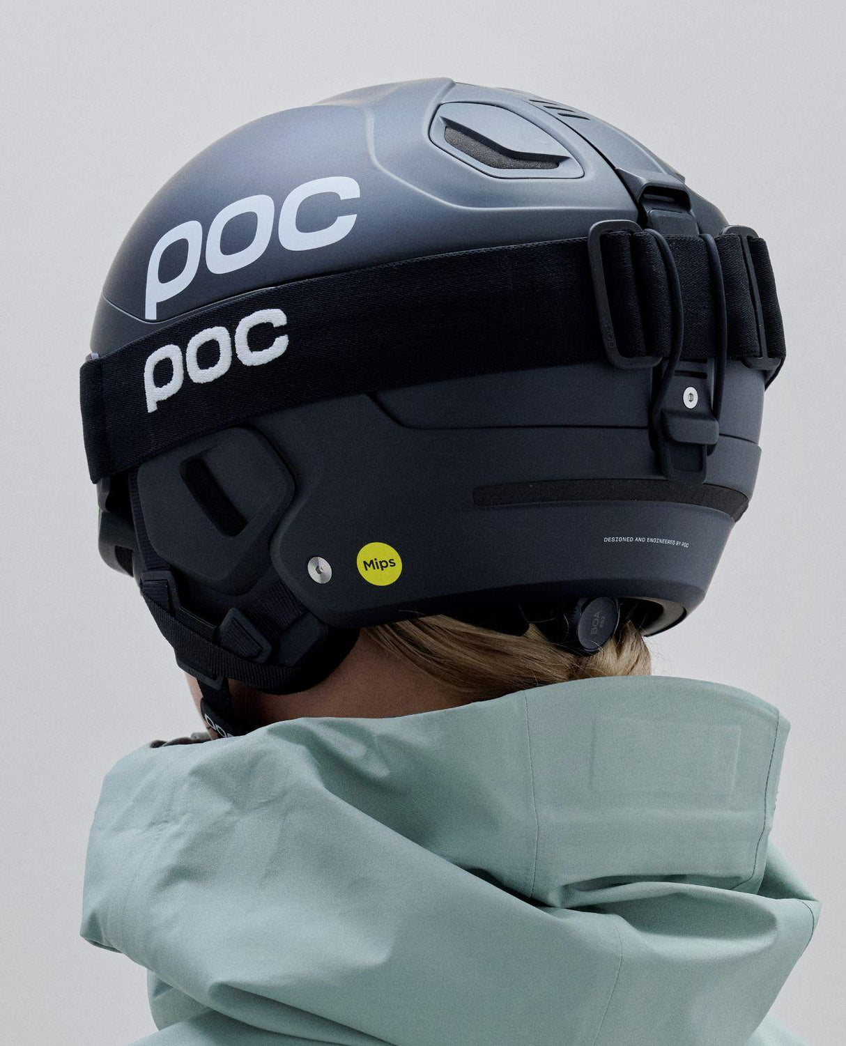 POC Nexal Mid skidglasögon i Uranium Black med tillhörande hjälm sett bakifrån mot en ljus bakgrund.