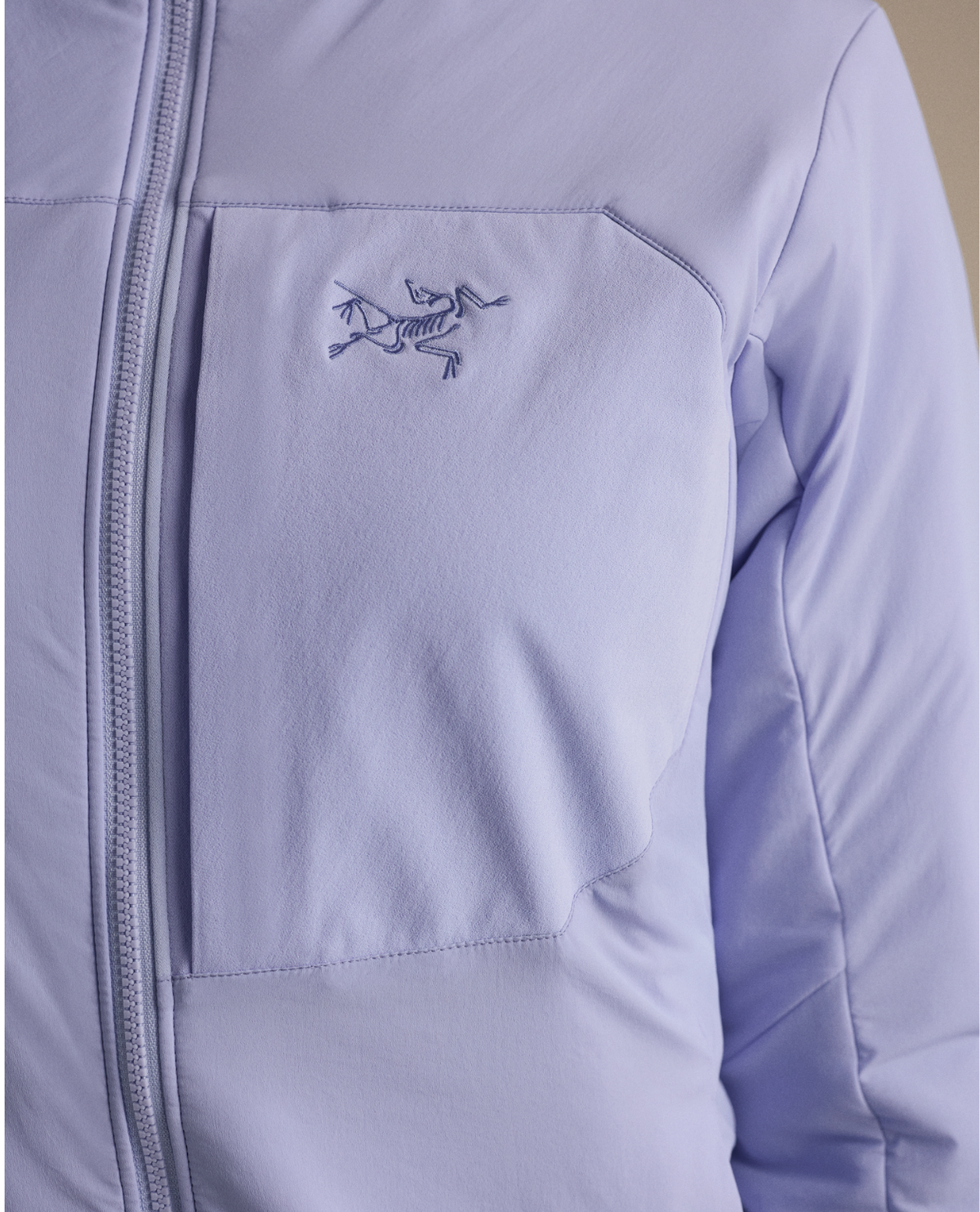 Närbild på Arc'teryx Proton Hoody dam i den lila färgen Kasumi, med fokus på bröstficka och logotyp.