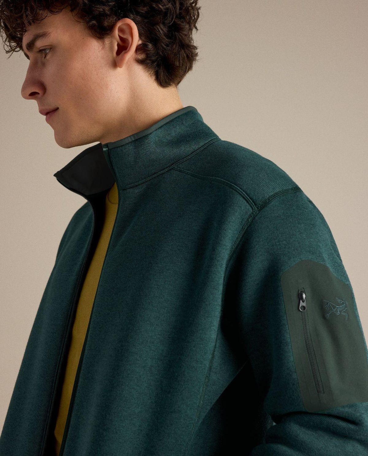 Manlig modell iförd Arc'teryx Covert Cardigan i färgen Dark Jade Heather med dragkedja och ärmficka.