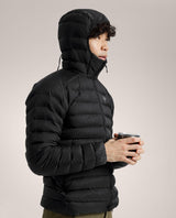 Manlig skidåkare i profil iförd den svarta dunjackan Arc'teryx Cerium Hoody med uppdragen huva och kopp i handen.