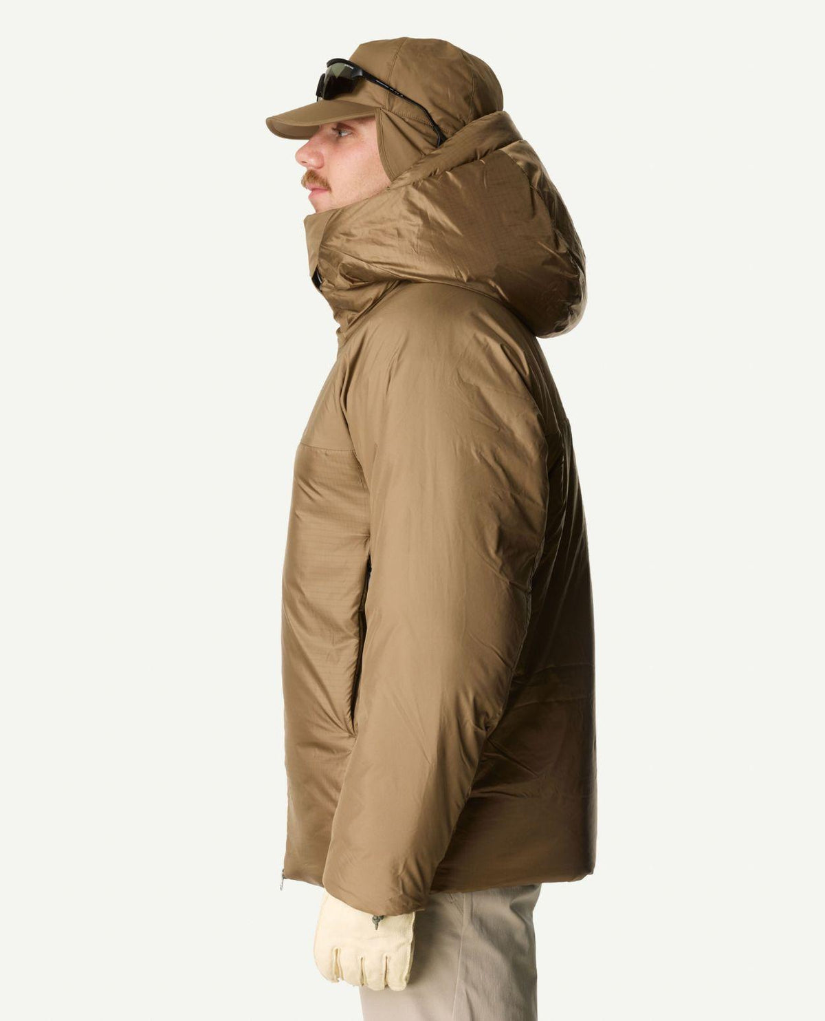 En person i profil som bär Houdini Double Dunfri skidjacka i brunt med huva och keps.