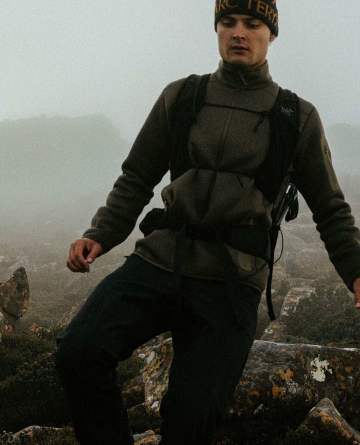 Man i bergslandskap iklädd Arc'teryx Covert Cardigan i färgen Mongoose Heather och en ryggsäck.